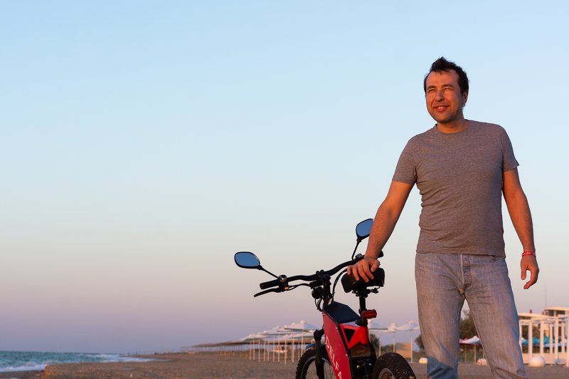 Daniel Tonkopiy with an early red Delfast bike on a beach at sunset