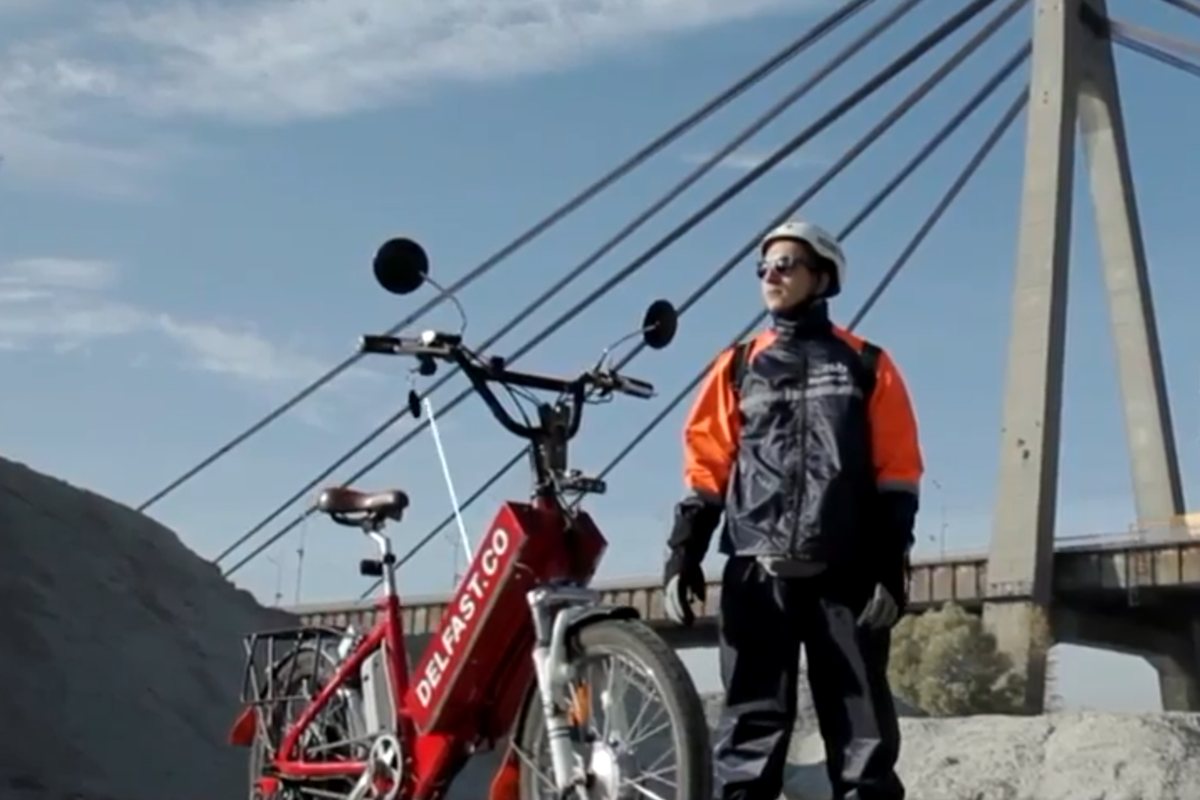 A Delfast courier beside a branded red delivery e-bike in Kyiv